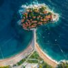Stunning aerial photo of a coastal island with turquoise waters and vibrant roofed buildings.