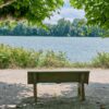 Peaceful bench by a tranquil lake under green trees, perfect for reflection and relaxation.