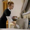 A housekeeper in uniform adjusts pillows in a luxurious hotel room, ensuring comfort and cleanliness.