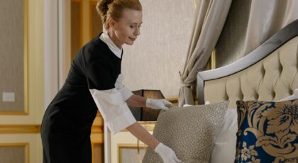 A housekeeper in uniform adjusts pillows in a luxurious hotel room, ensuring comfort and cleanliness.