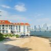 White beachfront hotel overlooking Panama City skyline and ocean under a blue sky.