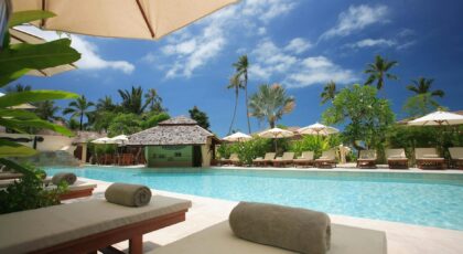 Experience ultimate relaxation at a sunlit tropical poolside resort featuring palm trees and blue skies.