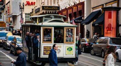 Iconic San Francisco cable car with passengers on a vibrant urban street, showcasing transportation and city life.