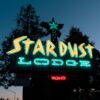 Vibrant neon signage of Stardust Lodge in Tahoe City at dusk, surrounded by trees.