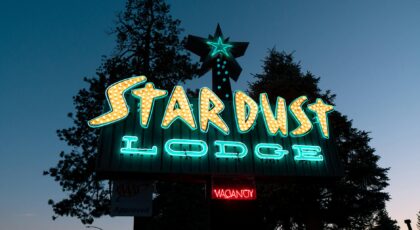 Vibrant neon signage of Stardust Lodge in Tahoe City at dusk, surrounded by trees.
