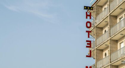 A modern hotel building with distinct balconies and a red sign against a clear blue sky.