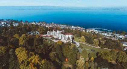 Scenic aerial view of a lakeside town with lush greenery and a grand hotel by the shore.